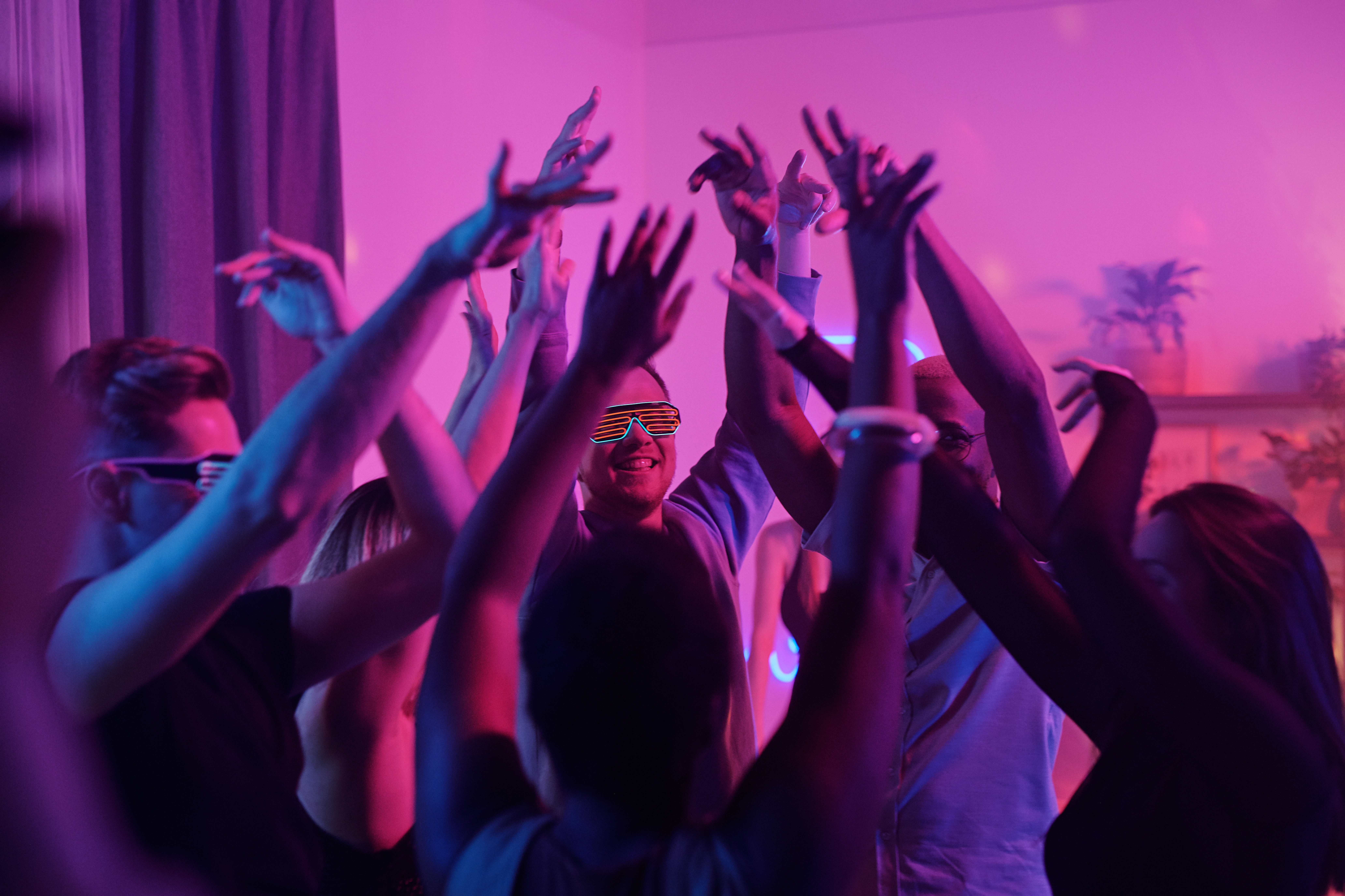 Young intercultural glamorous friends raising their arms while dancing at party